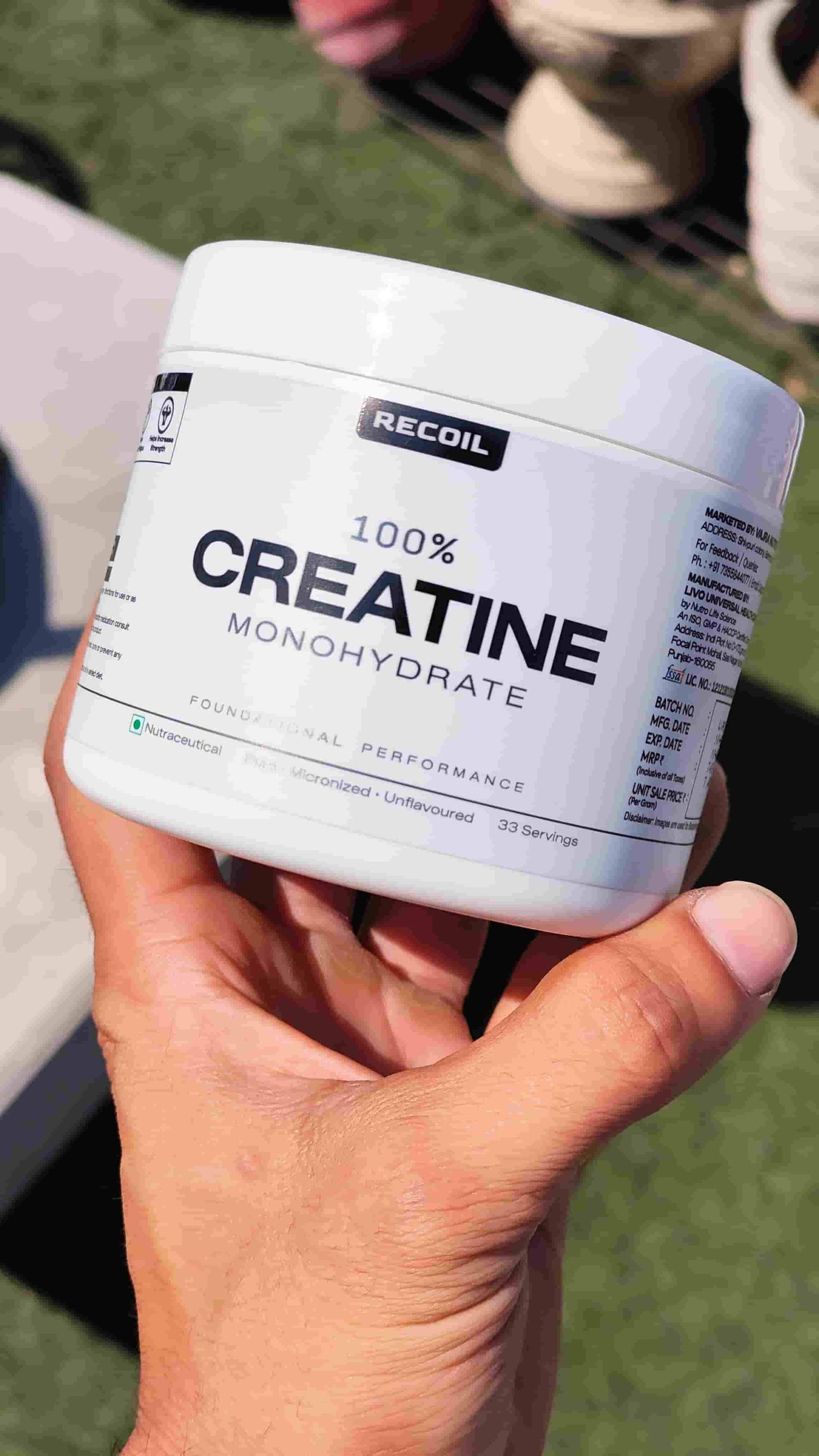 Hand holding a container of 'Recoil' 100% Creatine Monohydrate.