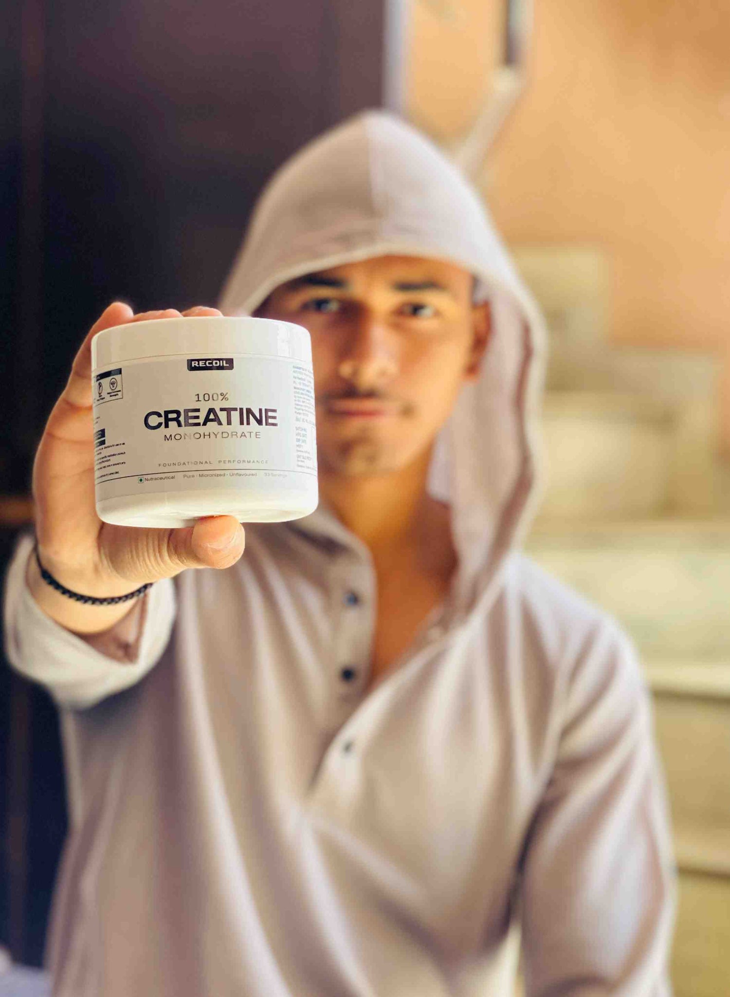 Person holding a container labeled 'Creatine' in front of a blurred background