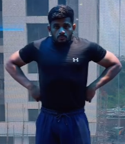Person wearing a black Under Armour t-shirt and blue pants standing in front of a large window with a cityscape view.
