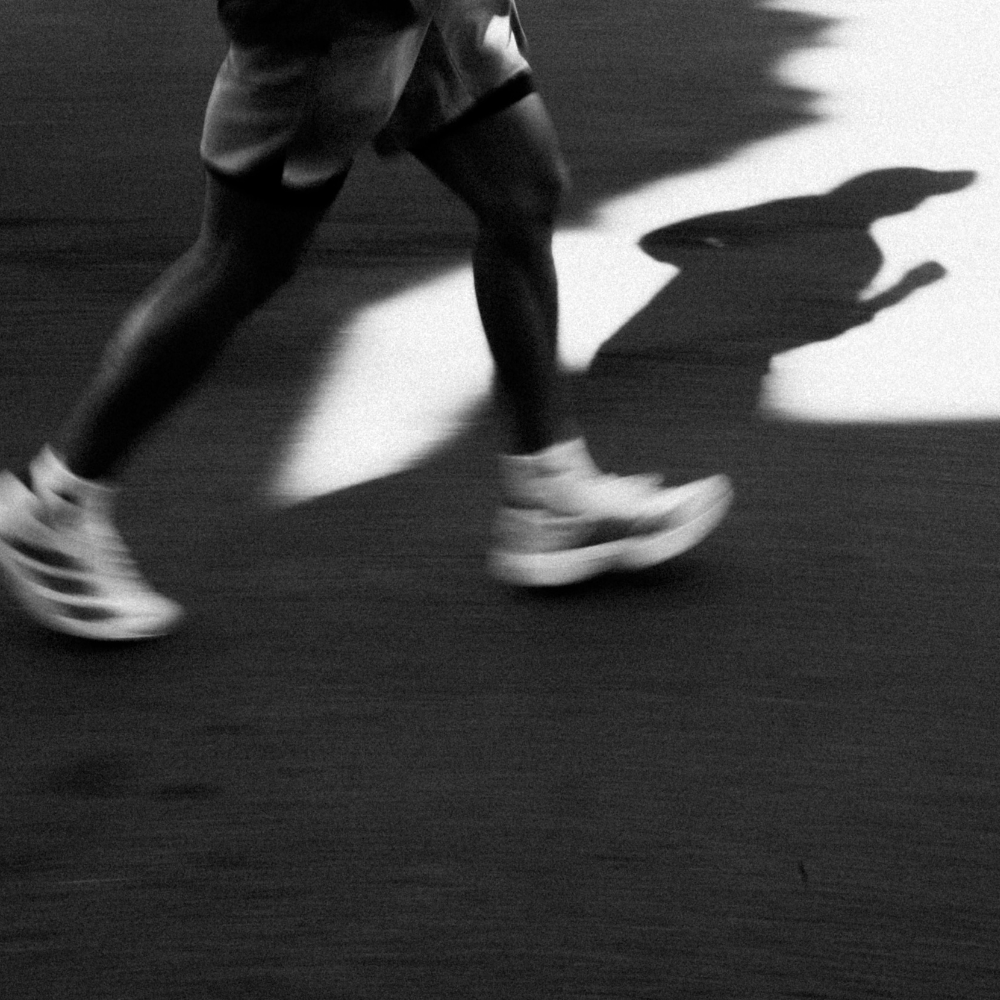 Black and white image of a person running with a shadow on the ground, recoil creatine monohydrate
